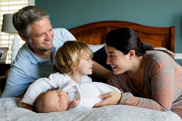 child and baby with parents on their bed